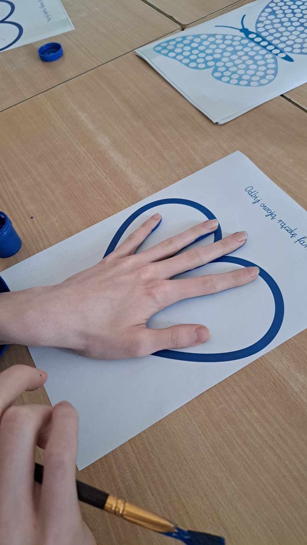 Na zdjęciu widać tylko dłoń jakiegoś ucznia, ktory odbija tę dłoń na kartce z niebieskim serduszkiem