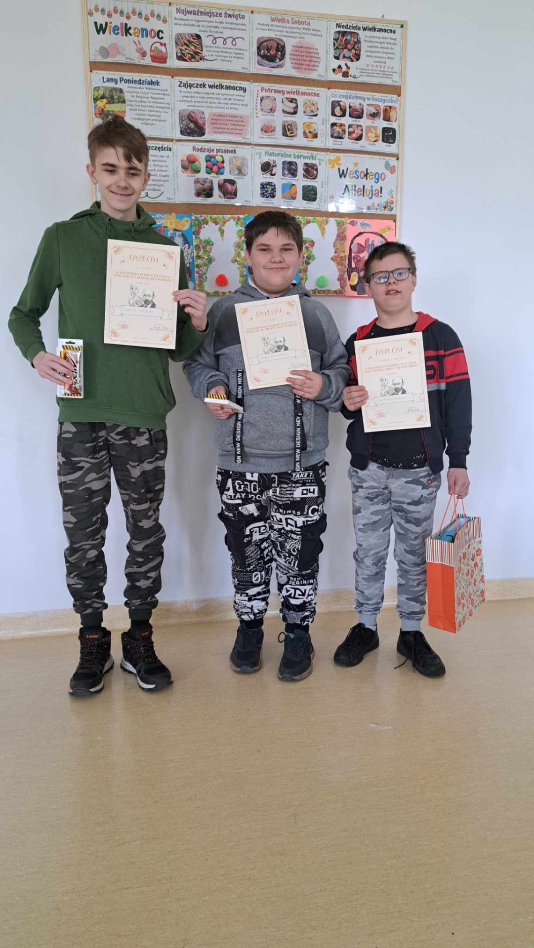 3 uczniów chłopców stoi z dyplomami i nagrodami