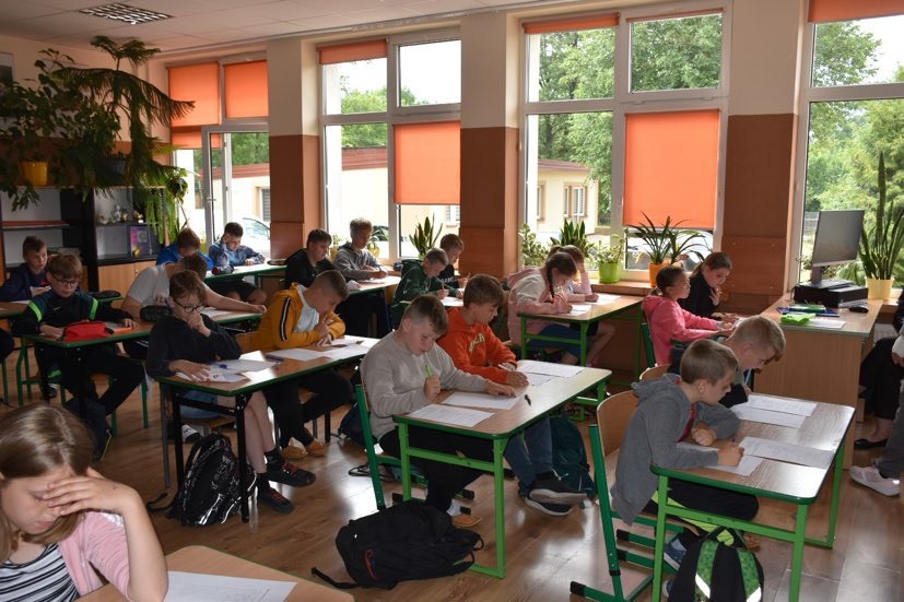 Uczniowie siedzą w ławkach i piszą test egzaminacyjny