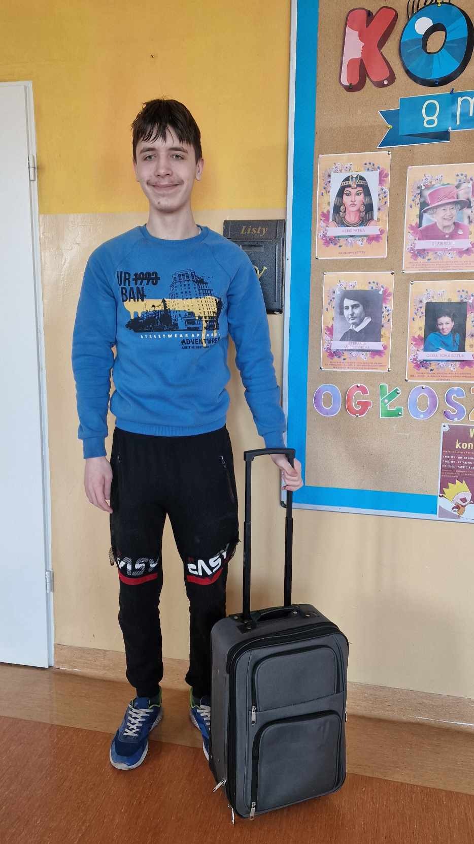 Uśmiechnięty nastolatek pozuje z walizką na kółkach