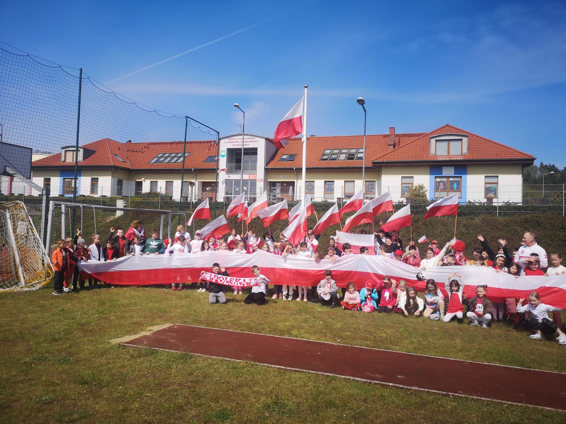 Grupa ludzi w biało-czerwonych strojach pozuje na tle budynku szkoły
