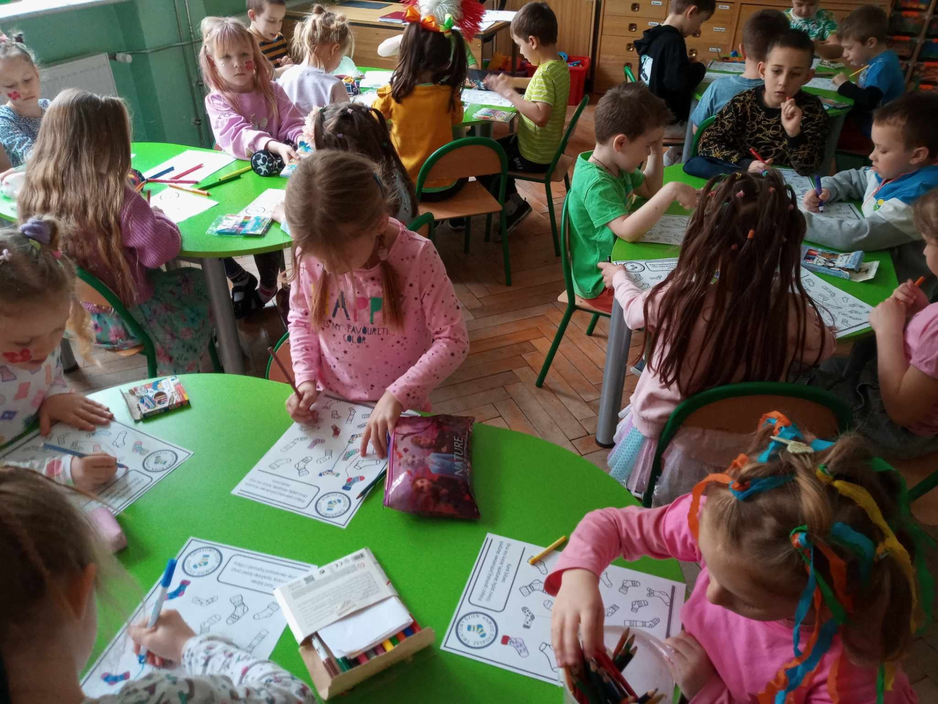 Uczniowie grupy 0 rozwiązują przy stolikach kartę pracy dotyczącą Dnia Kolorowej Skarpetki.