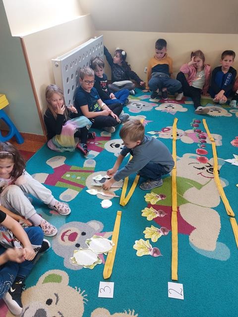 dzieci na dywanie z obrazkami warzyw i owoców