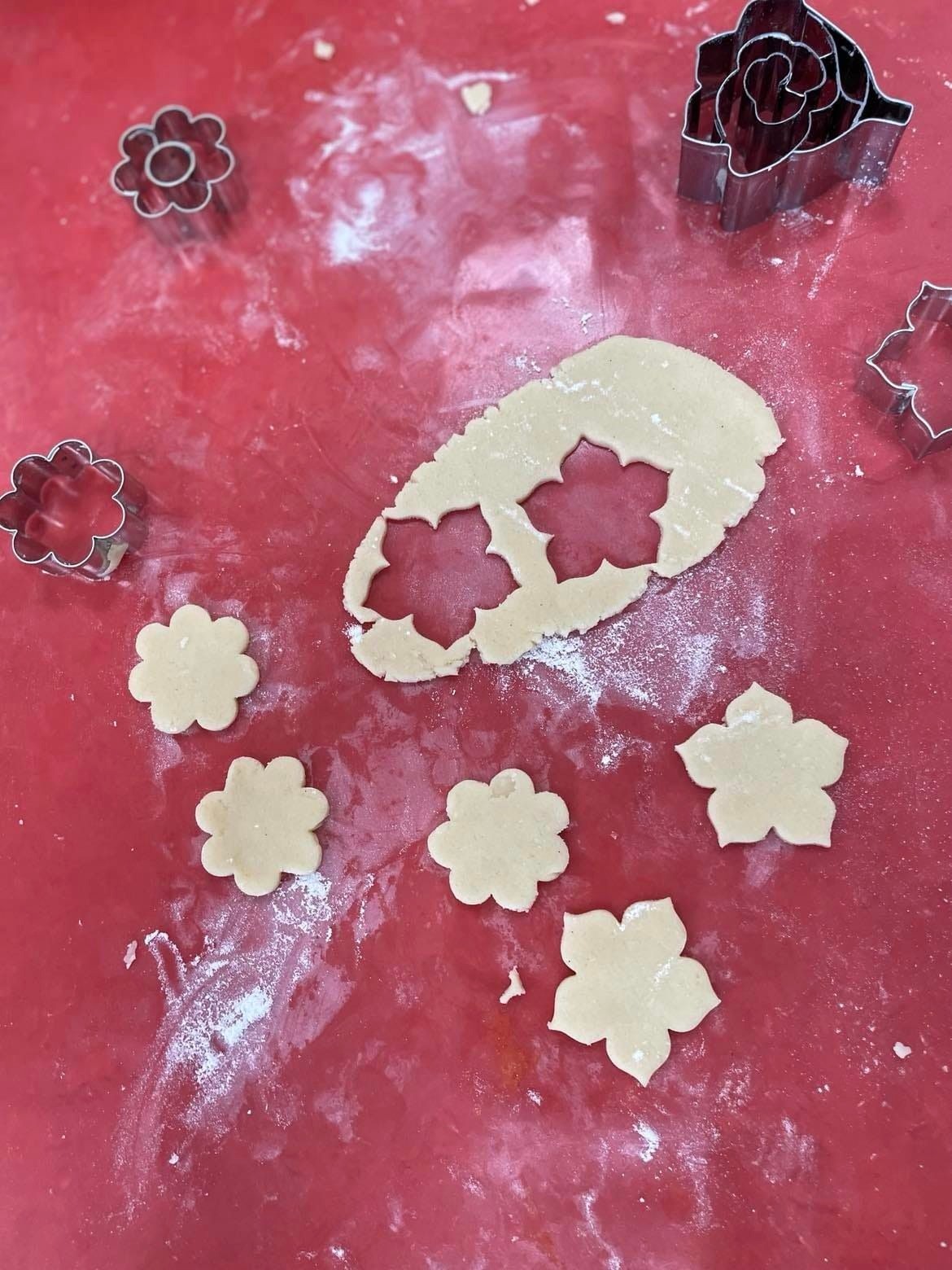 Na zdjęciu widzimy czerwony blat kuchenny, na którym znajdują się różne metalowe foremki do ciastek w kształtach kwiatów oraz jedna w kształcie róży.