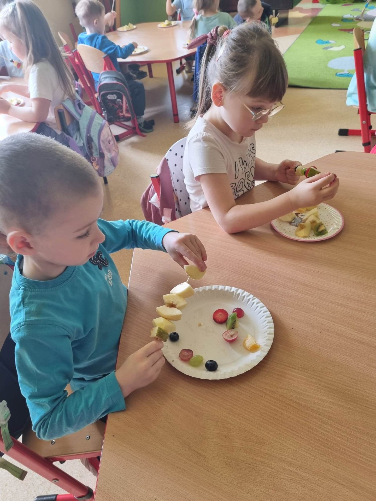 Przedszkolaki przygotowują zdrowe szaszłyki przy stoliku przedszkolnym