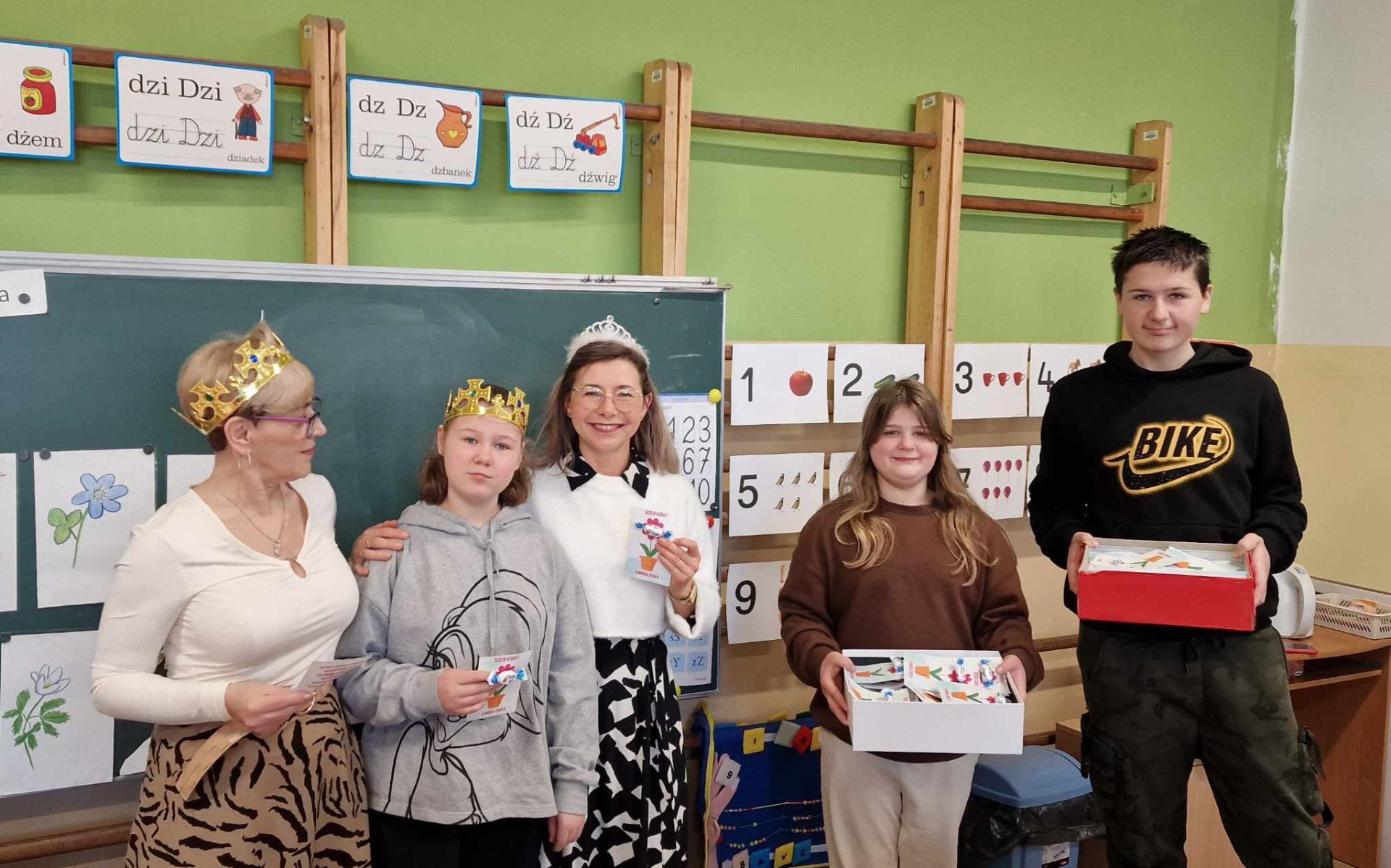 Przedstawiciele samorządu uczniowskiego pozują do zdjęcia z nauczycielkami i uczennicami, które mają na sobie korony.