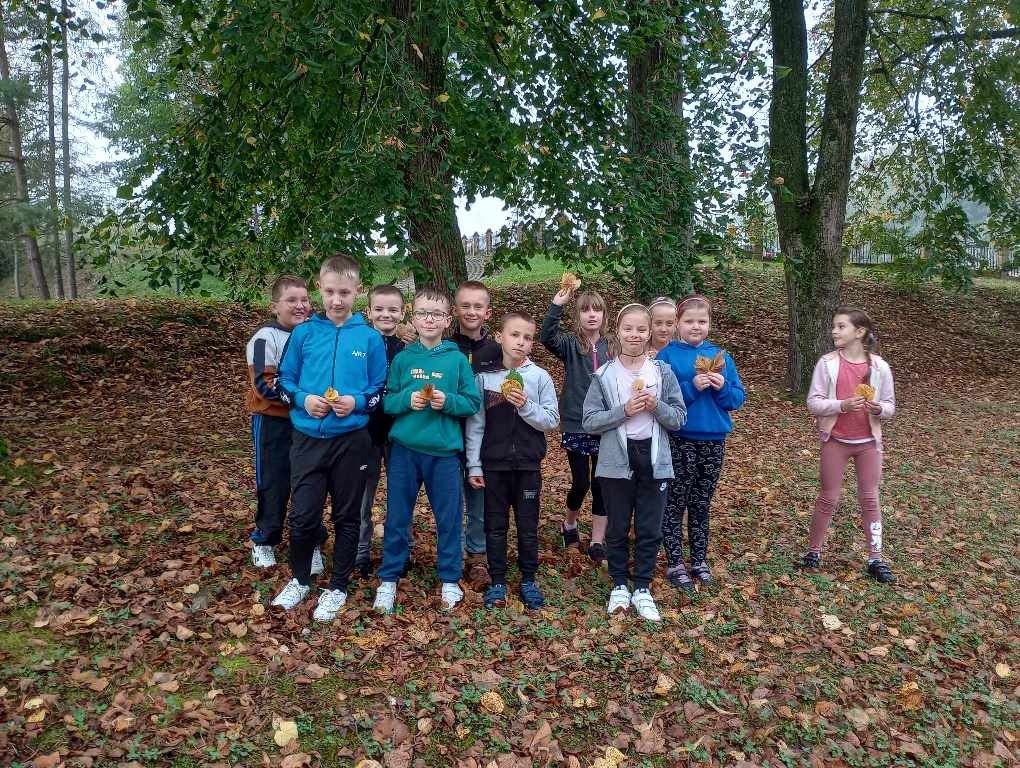 Jedenaścioro uczniów kl.IIIa , sześciu chłopców i pięć dziewczynek, z kolorowymi liśćmi przed lasem.